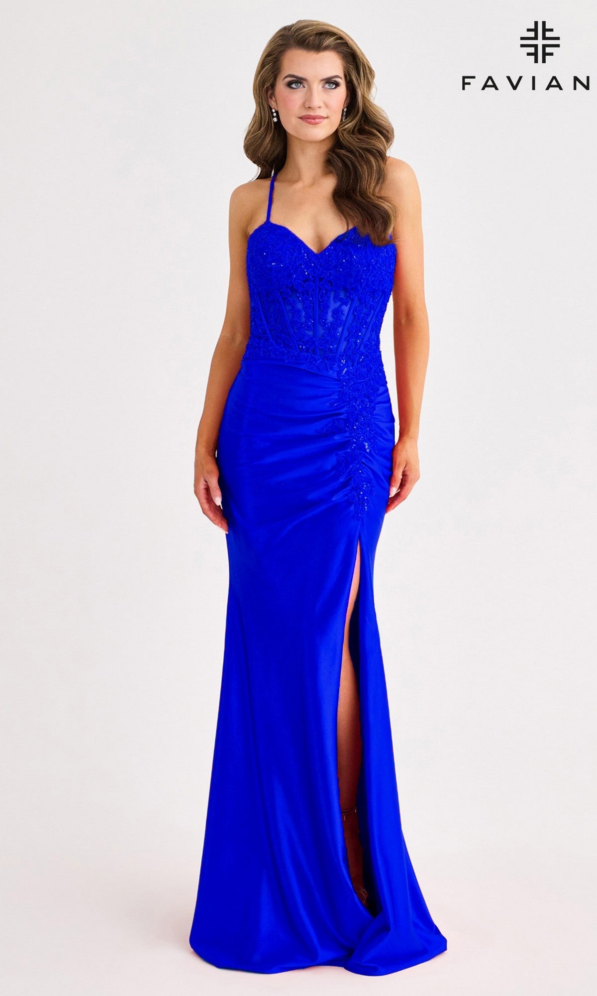 A woman wears the Faviana 11414 long prom dress in bright blue satin, featuring spaghetti straps, a sweetheart neckline, beaded bodice, lace embroidery at the ruched waist, and a thigh-high slit. Faviana logo in the top right corner.